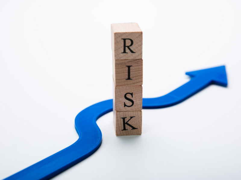 Holzklötze formen das Wort Risk, Blauer Pfeil im Hintergrund